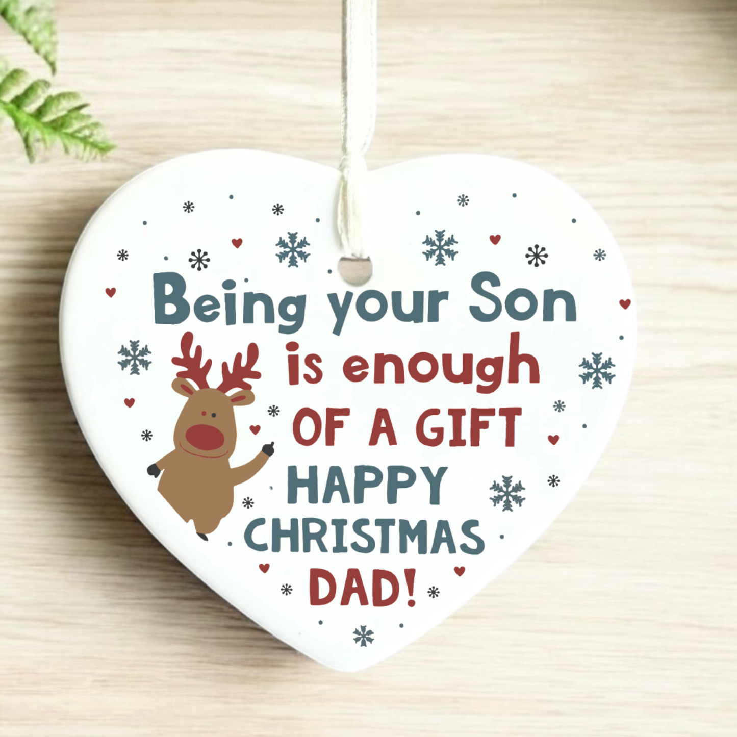 Heart-shaped Christmas ornament with text and reindeer illustration on a wooden surface