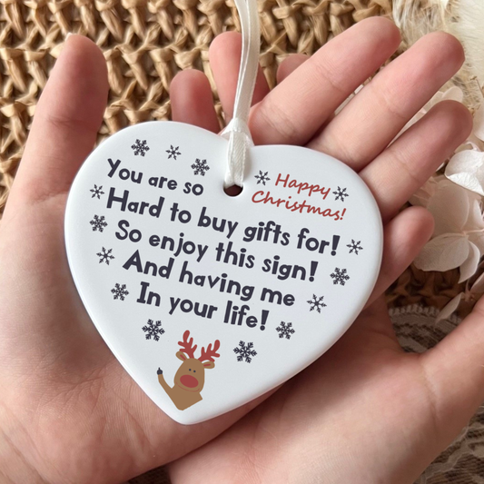 Heart-shaped ornament with text and a reindeer illustration held in a hand against a textured background.