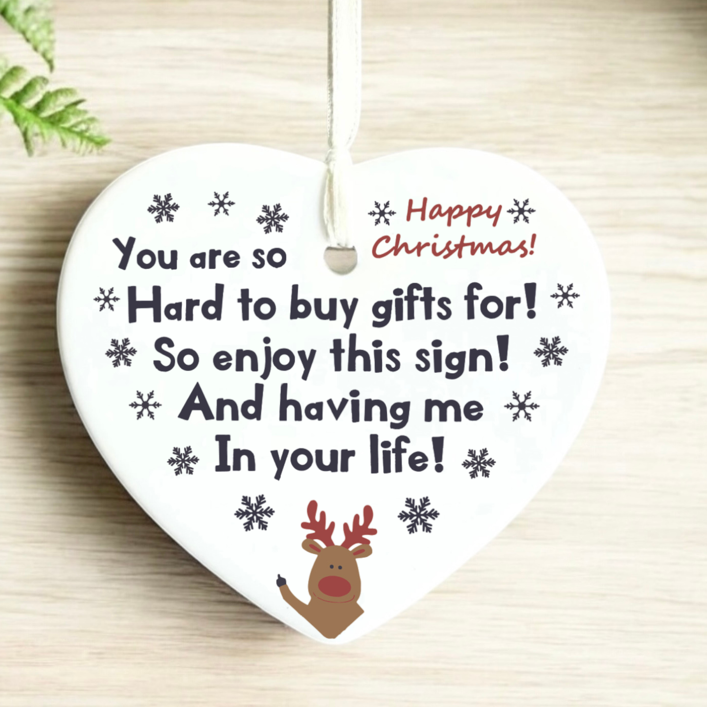 Heart-shaped Christmas ornament with humorous text and reindeer design on a wooden background