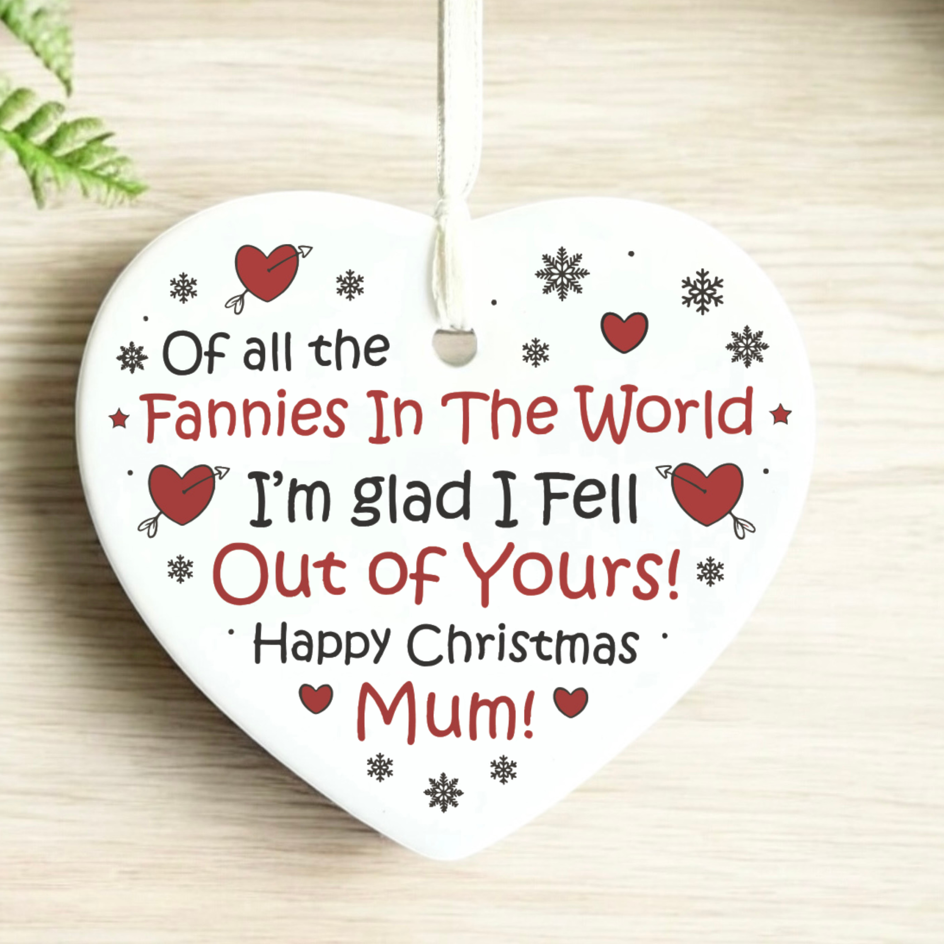 Heart-shaped Christmas ornament with humorous message for 'Mum' on a wooden surface.