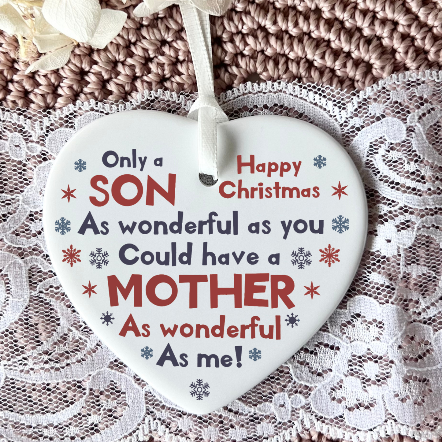 White ceramic heart-shaped Christmas ornament held in a hand as shown in 31.jpg. The ornament features red and blue snowflakes with the printed text: Only a SON As wonderful as you Could have a MOTHER As wonderful As me! Happy Christmas. It hangs from a delicate white ribbon.