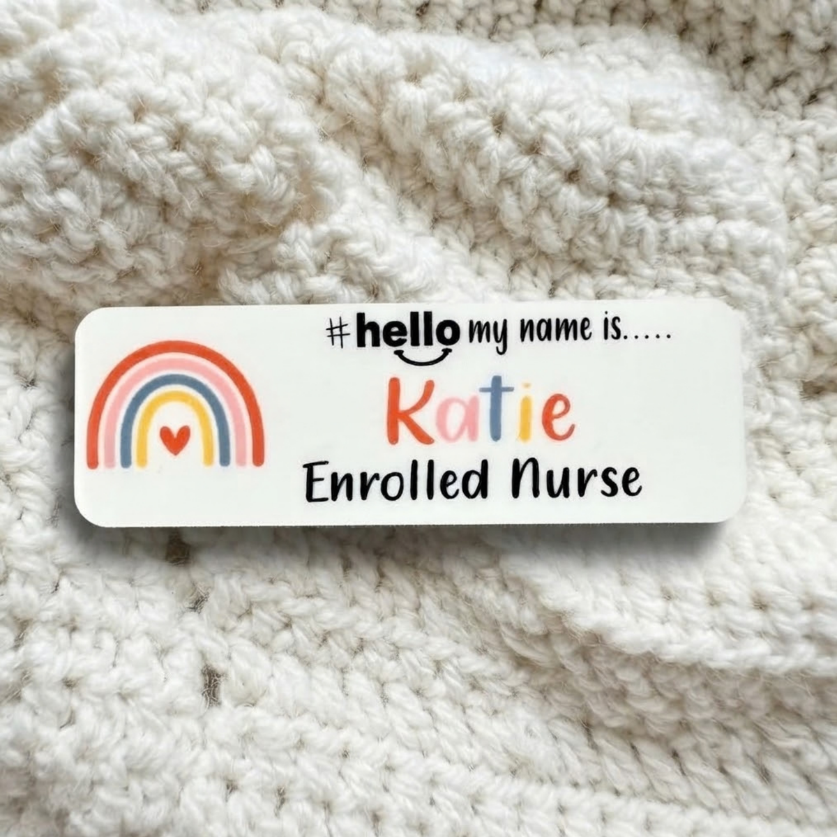 A personalized white rectangular name tag with a colorful rainbow graphic and the text '#hello my name is.