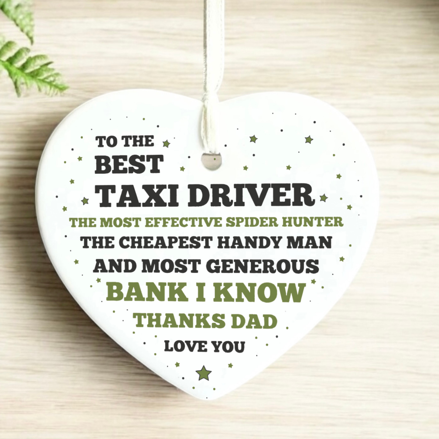  white ceramic heart-shaped ornament featuring a funny thank you message to a dad, with text highlighting his roles as a taxi driver, spider hunter, handyman, and bank, finished with a white ribbon.