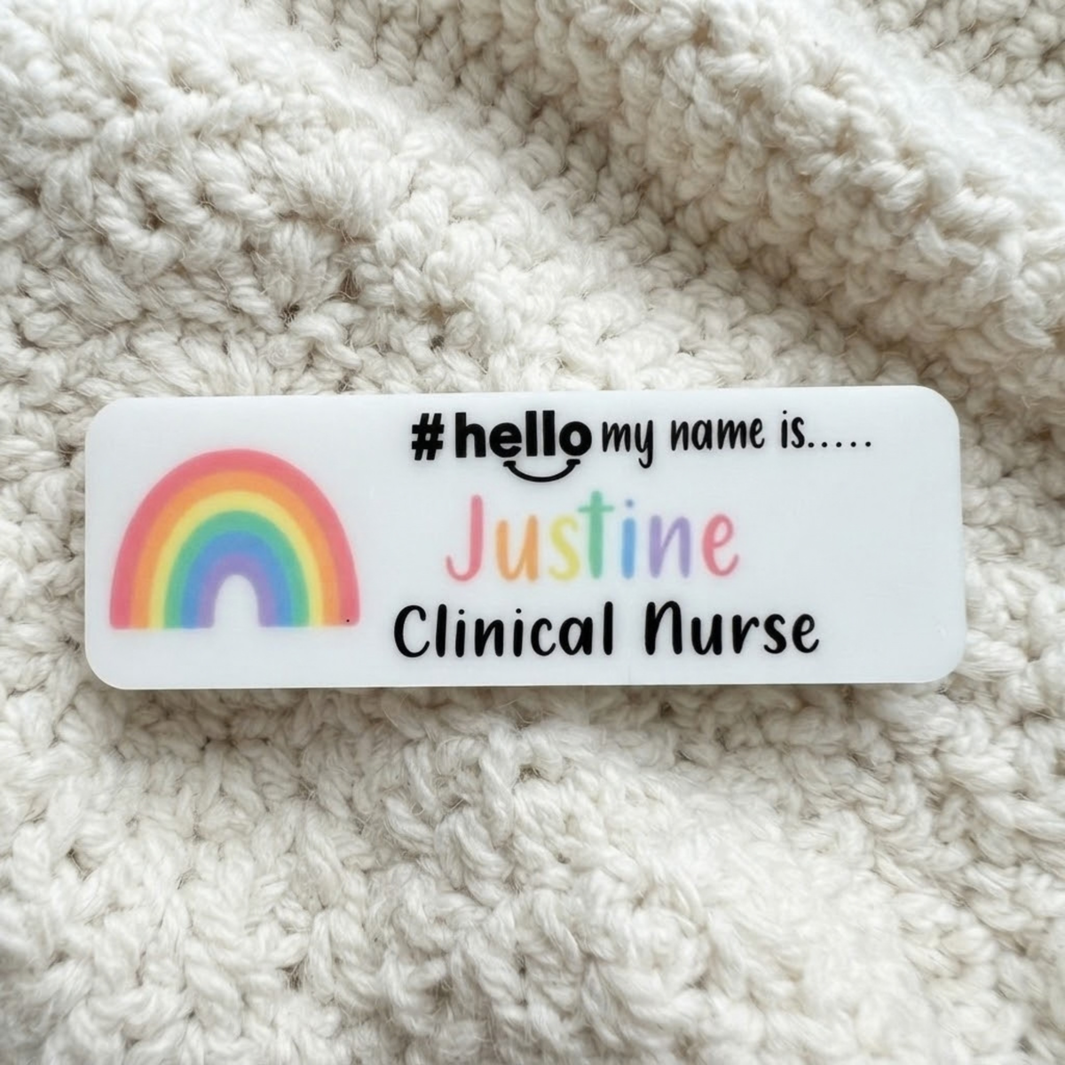 A rectangular white sticker with rounded corners featuring a colorful rainbow graphic and the text '# hello my name is.