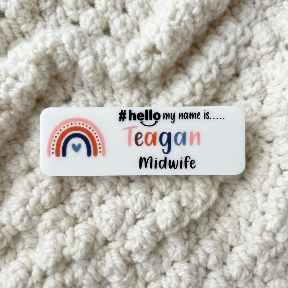 A white rectangular name tag with a colorful rainbow graphic and the text '# hello my name is.