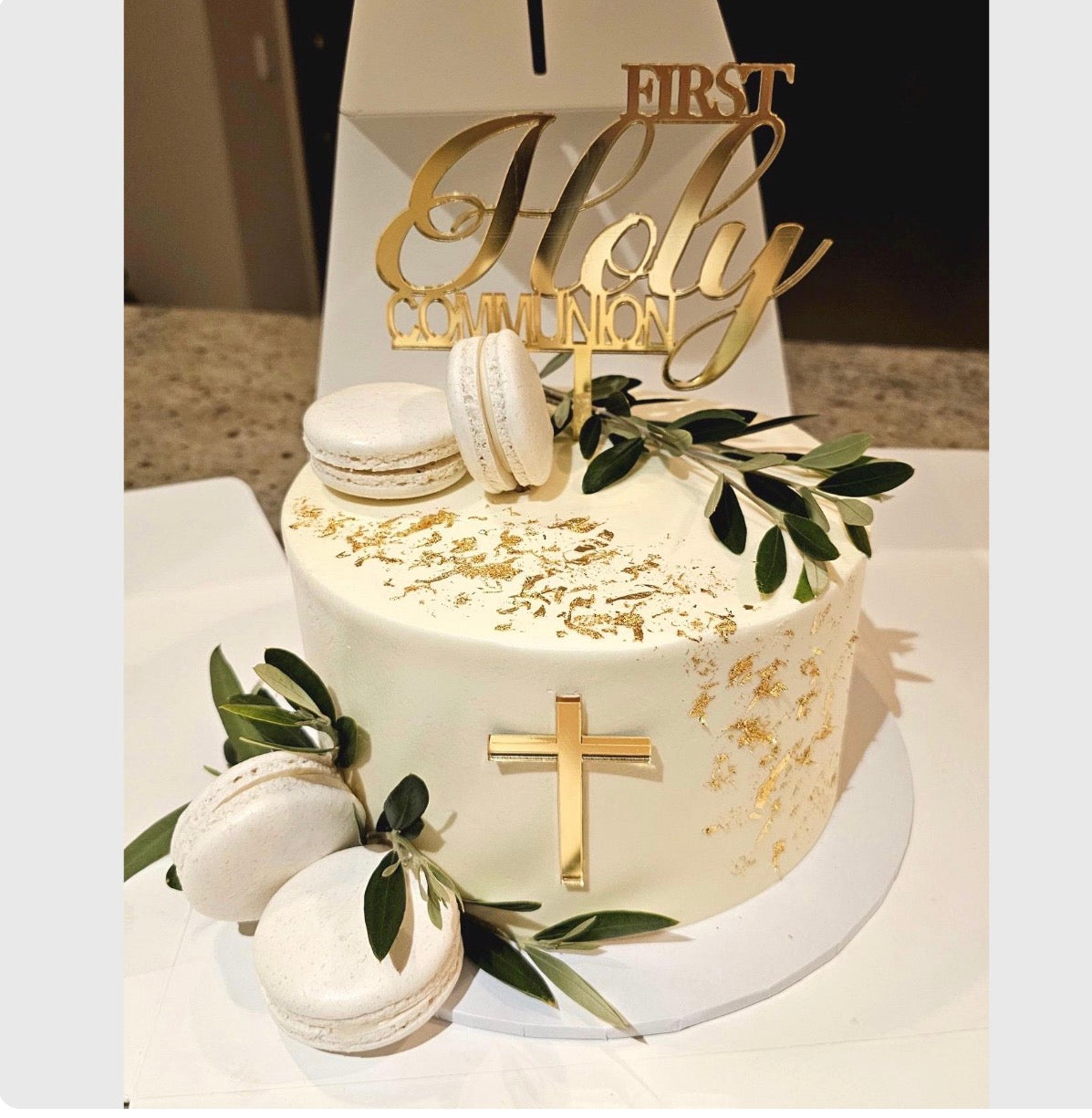 White cake with gold decorations and 'First Holy Communion' topper on a white plate.