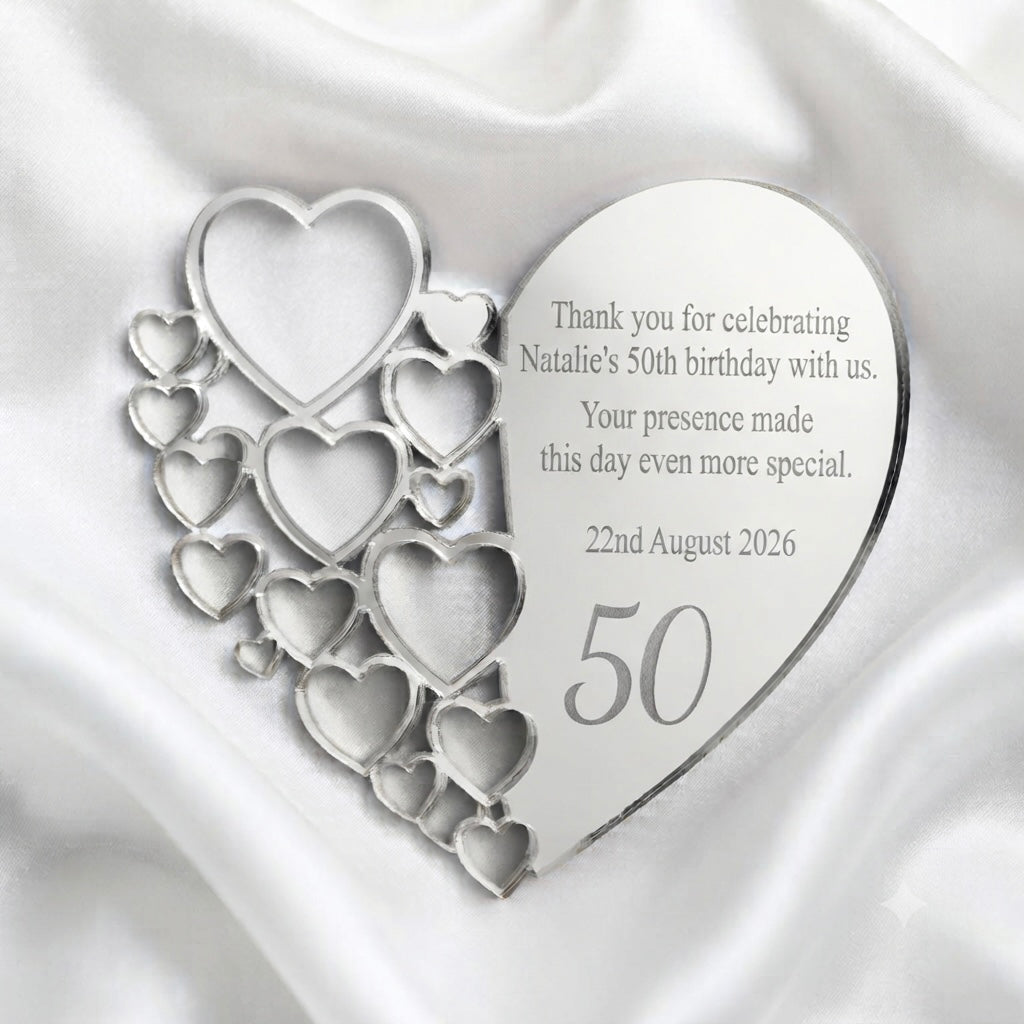 A heart-shaped silver keepsake plaque with a cascading pattern of smaller cutout hearts, placed on a draped white satin fabric. The main heart is engraved with a personalized birthday message for Natalie's 50th birthday, dated 22nd August 2026, with the number 50 prominently displayed.