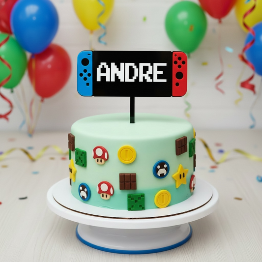 A custom Super Mario-themed birthday cake on a white cake stand, decorated with mint green frosting, classic pixel-art style game elements, and a custom name topper shaped like a Nintendo Switch console displaying the name 'ANDRE'.